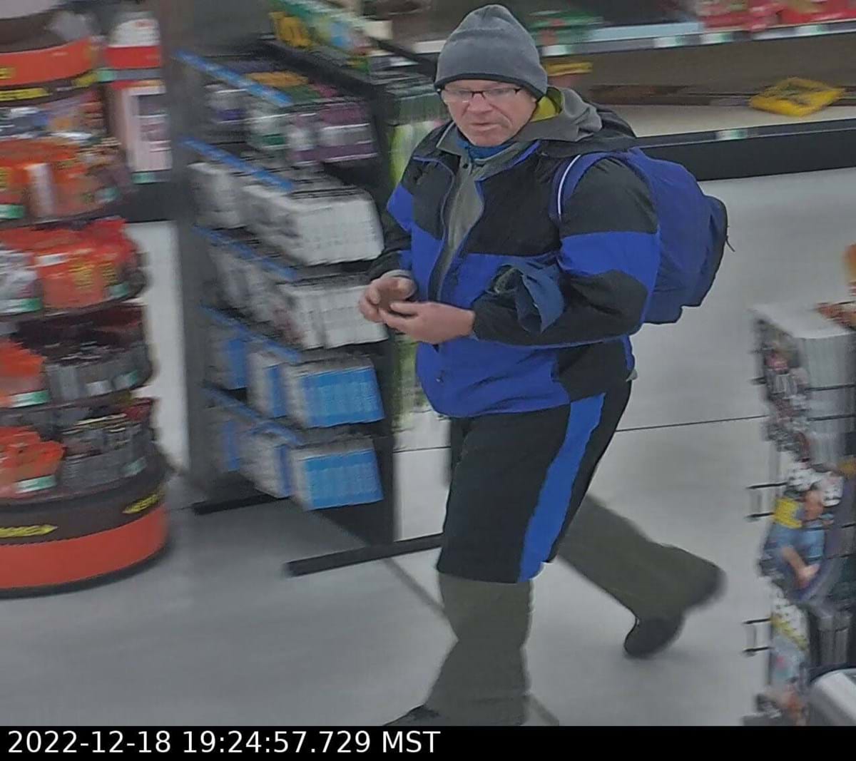 Man with blue and black winter coat on and a beanie walking through a store