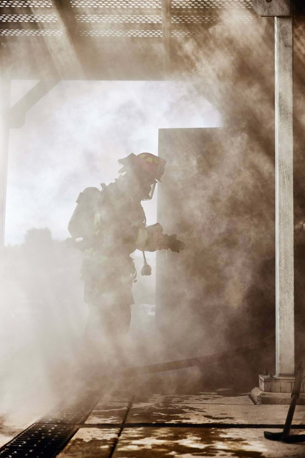 Silhouette of firefighter standing in a plume of smoke near building