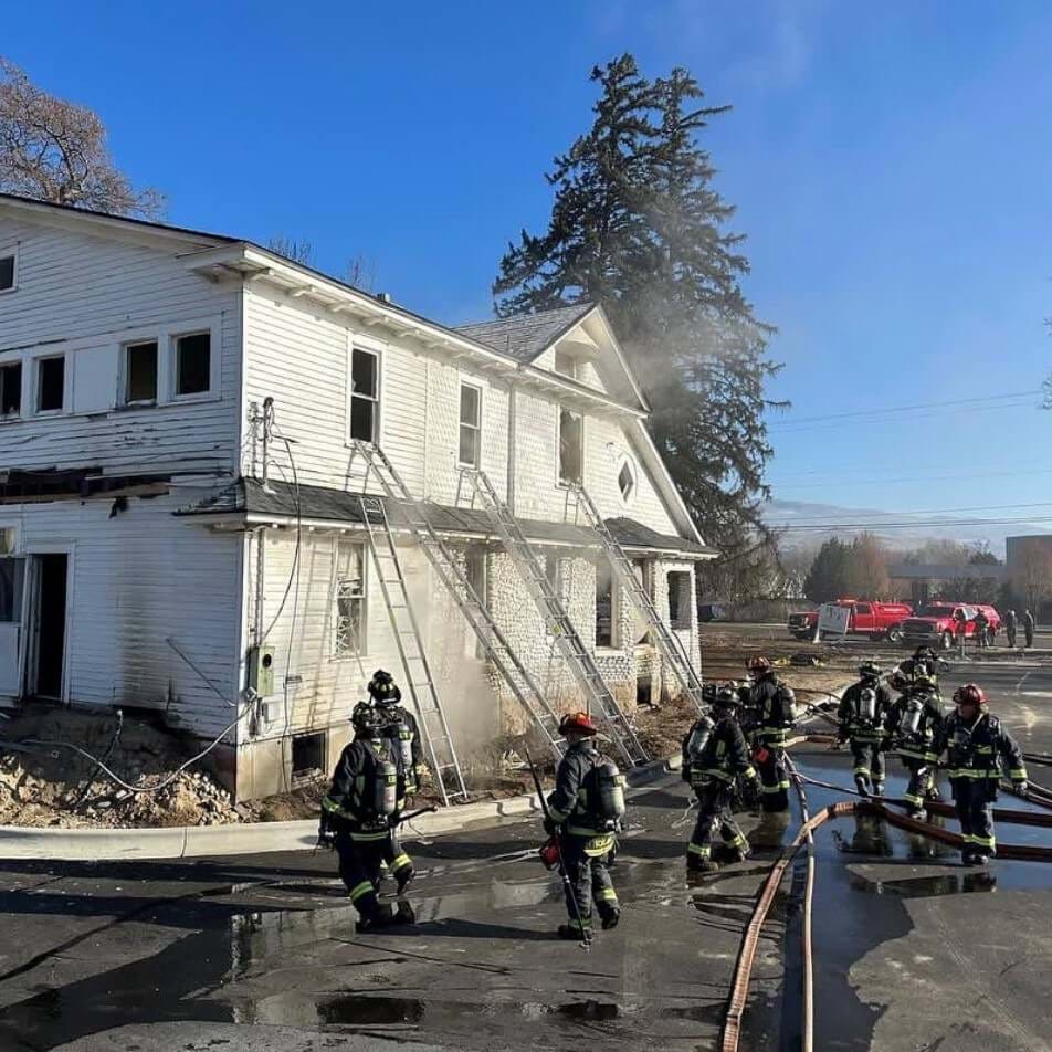 Firefighters trying to put a fire out on a large white house. 