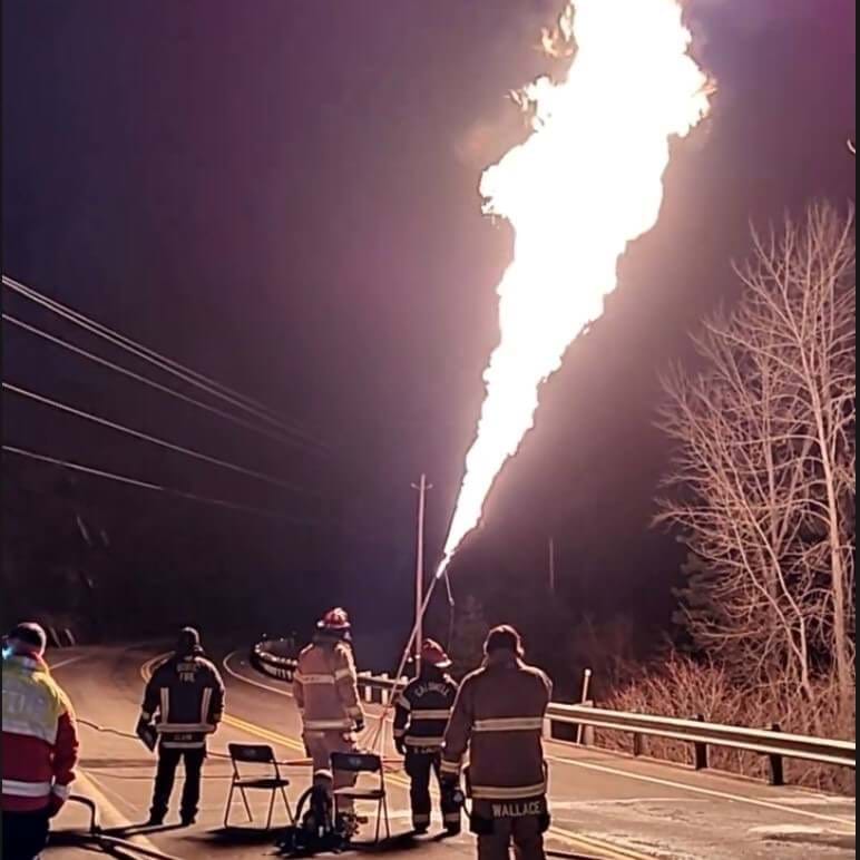 Firefighters at night wearing full gear with a giant flame in the sky.