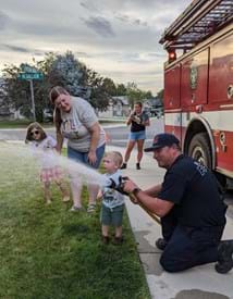 Firefighter kneeling down next to a fire truck showing kids the fire hose.