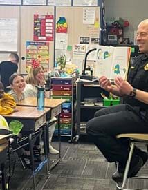 Firefighter in a classroom reading a book to a group of kids.