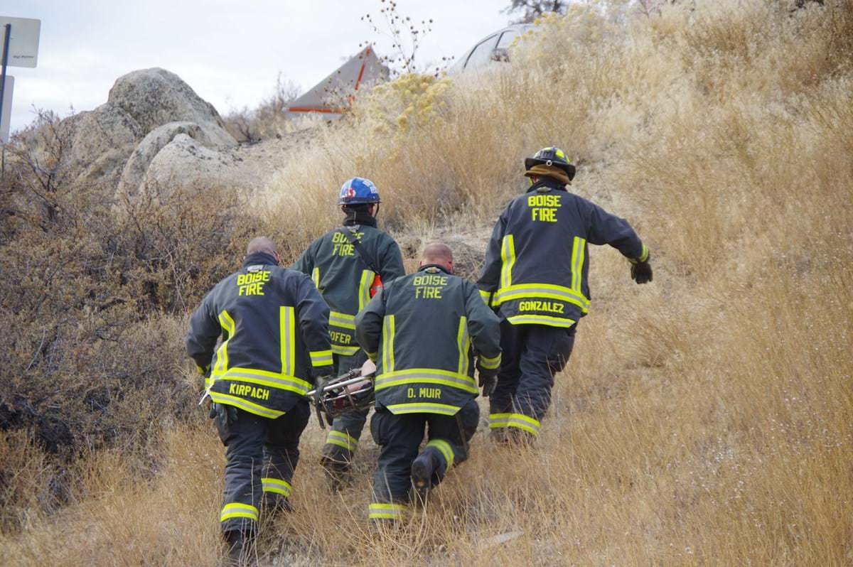 firefighters carrying a gurney up a hill covered in brush