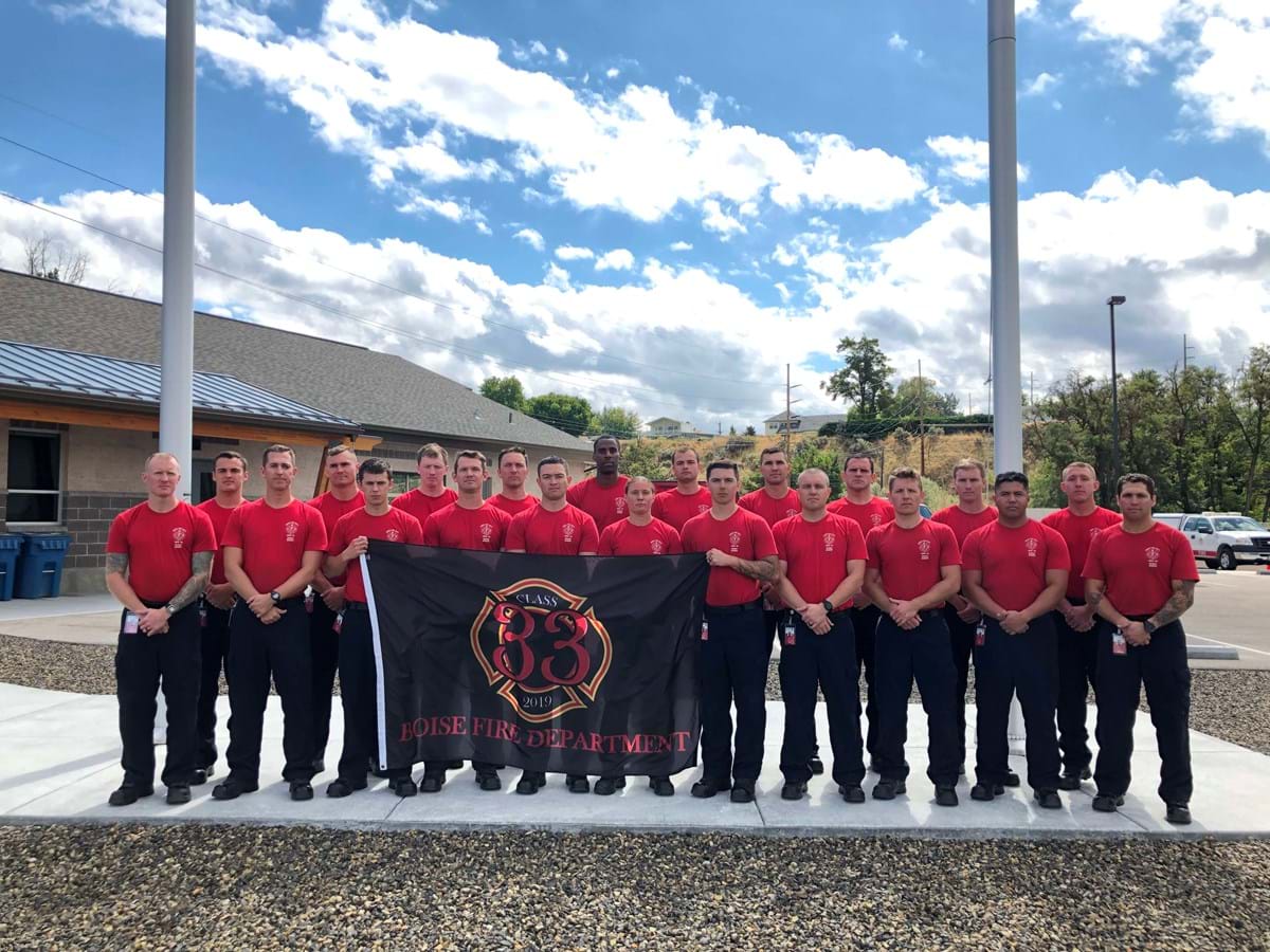 Firefighter recruits standing in front of fire department flag