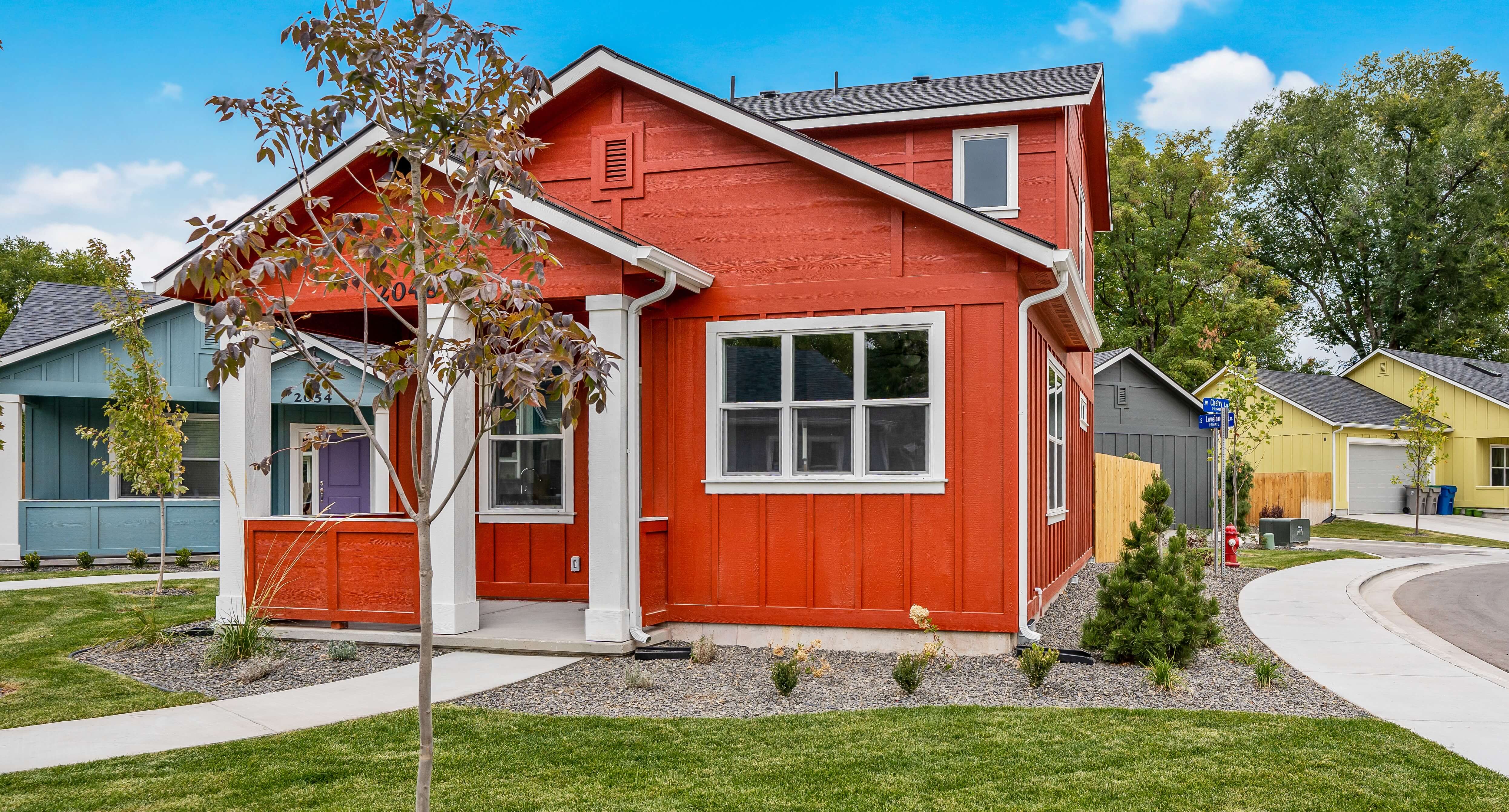 Red house with green grass in front and sidewalks running along the side.