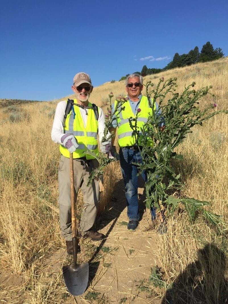 Two people standing on a trail holding a bundle of weeds