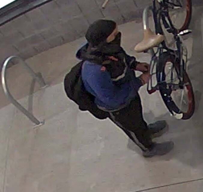 man with blue sweater, black hat, black mask and backpack standing near bike