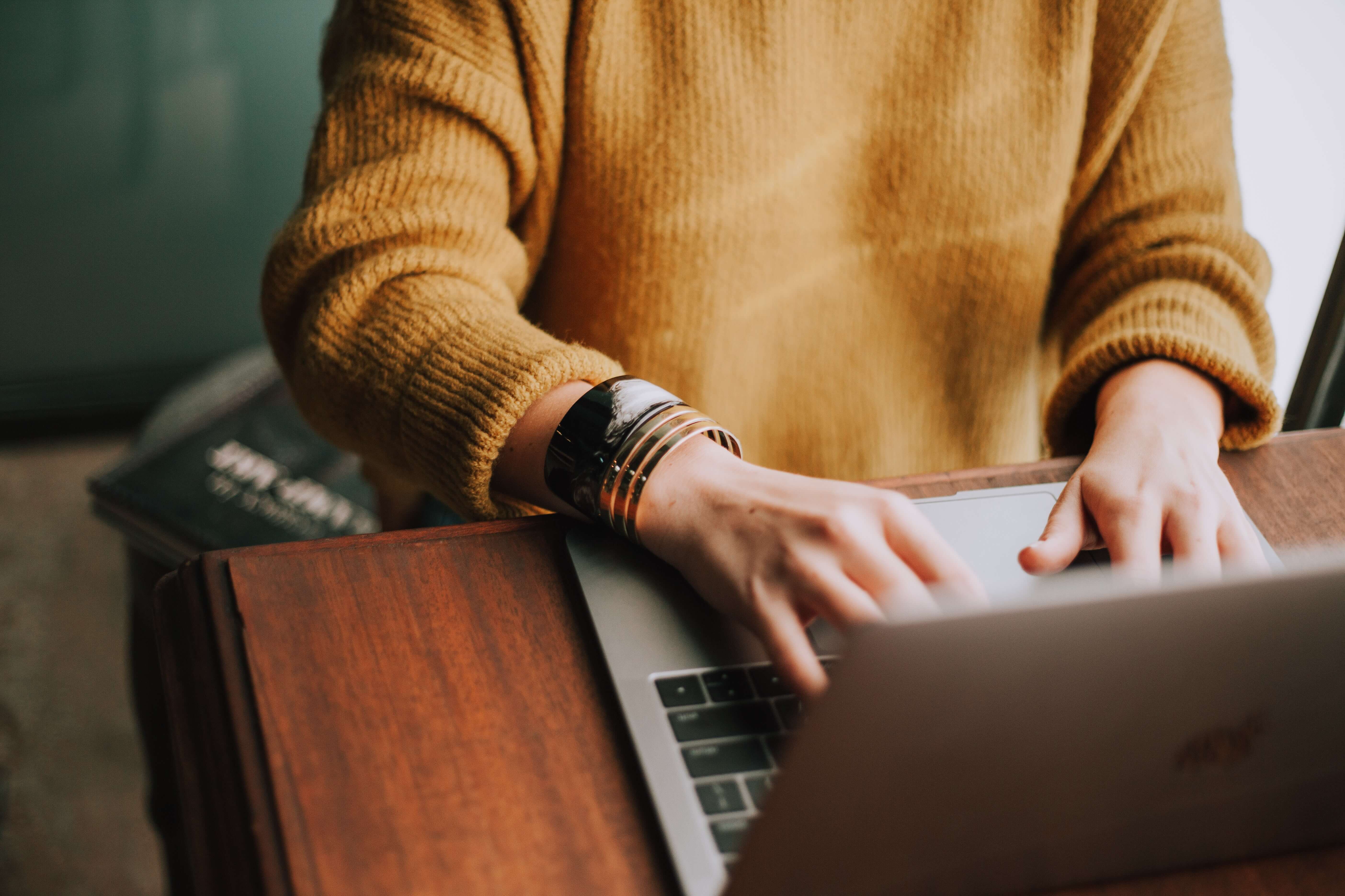 Person wearing a yellow sweater working on a laptop.