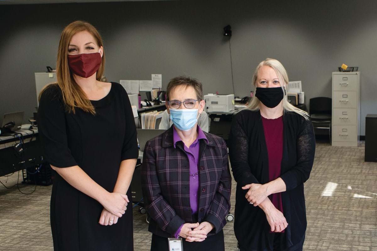 Three woman wearing masks stand together.