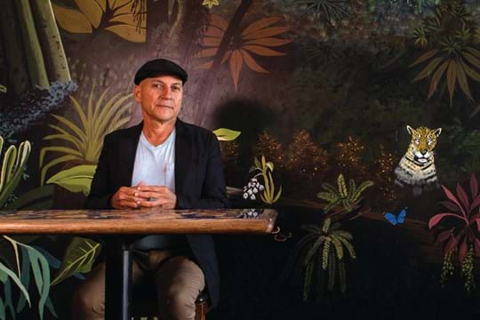 Man sitting at a table in a restaurant in front of a mural.