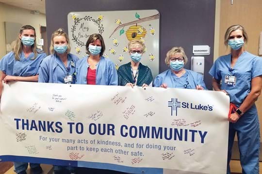 a line of health care workers holding a "thanks to our community" sign
