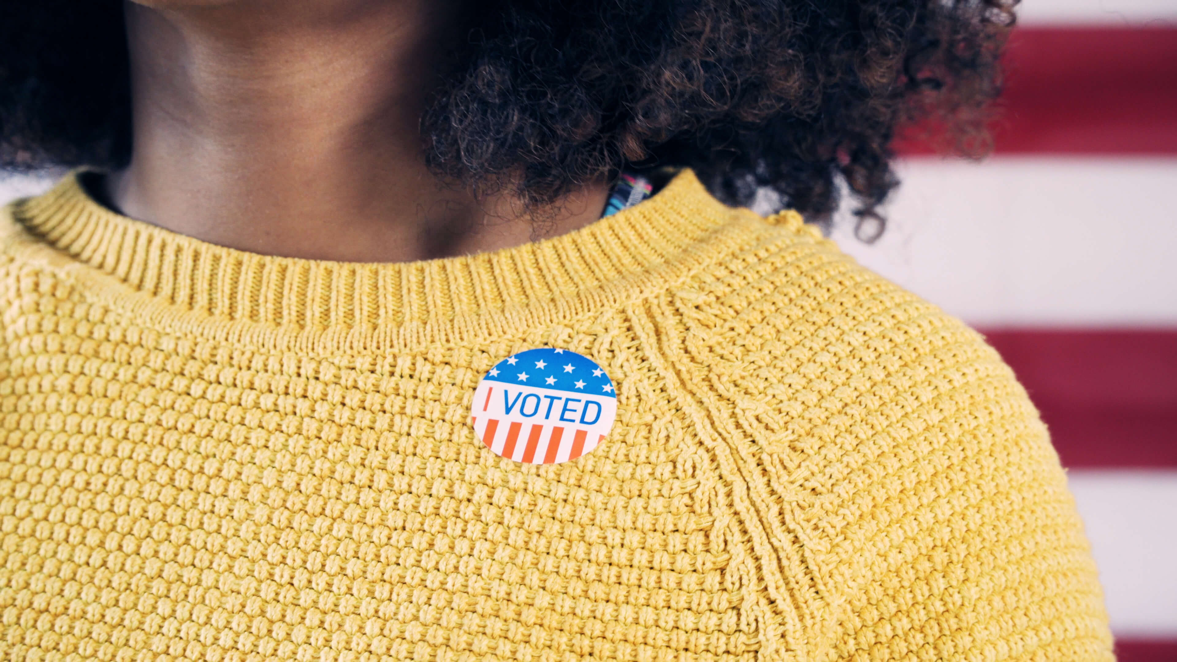 Woman wearing a yellow sweater and an "I Voted" sticker