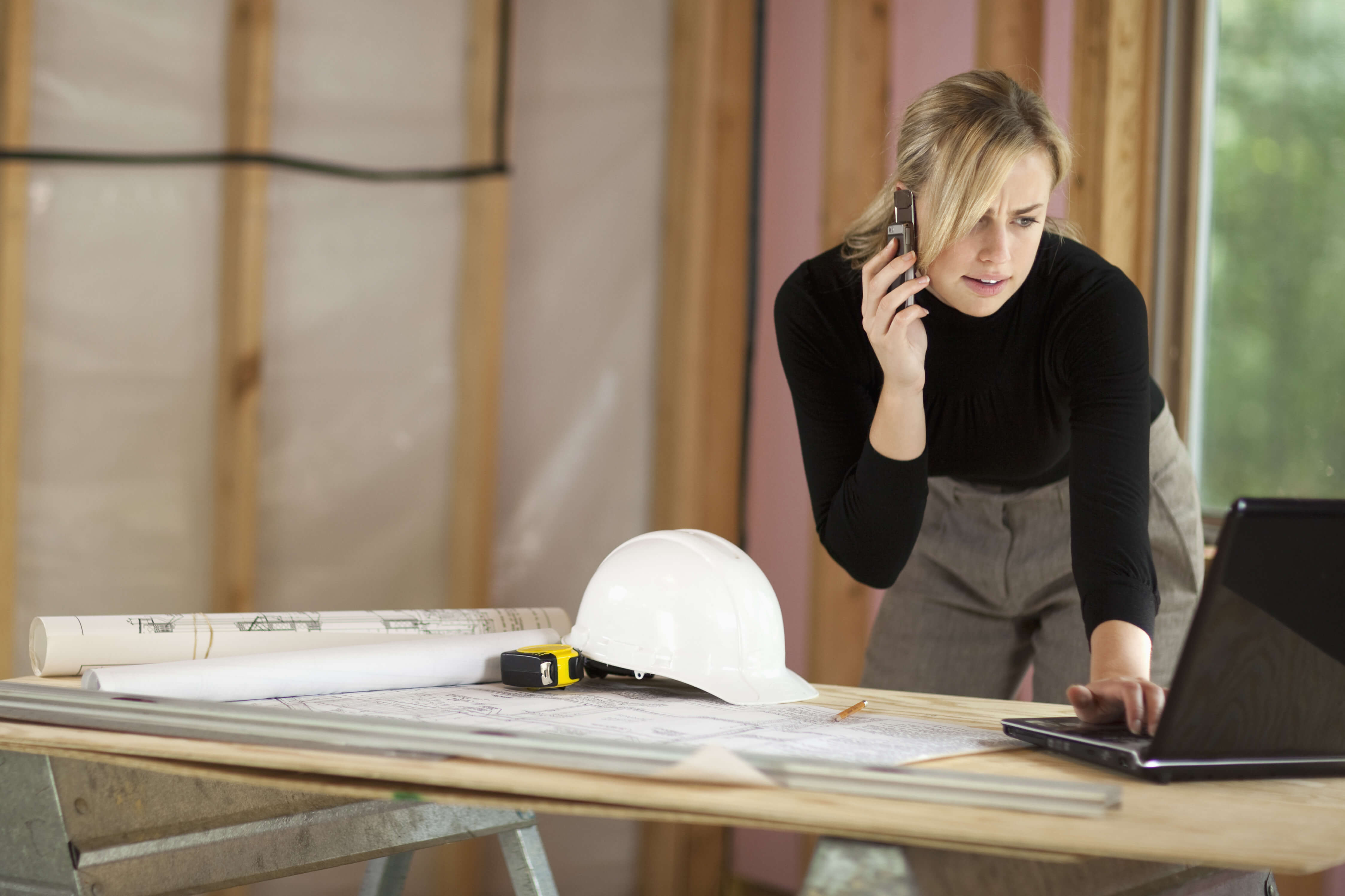 Woman standing at desk looking at computer while talking on the phone.