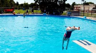 girl jumping off diving board into pool during the summer.