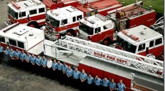 Aerial photo of fire ladder truck and four fire engines with crew of firefighters.