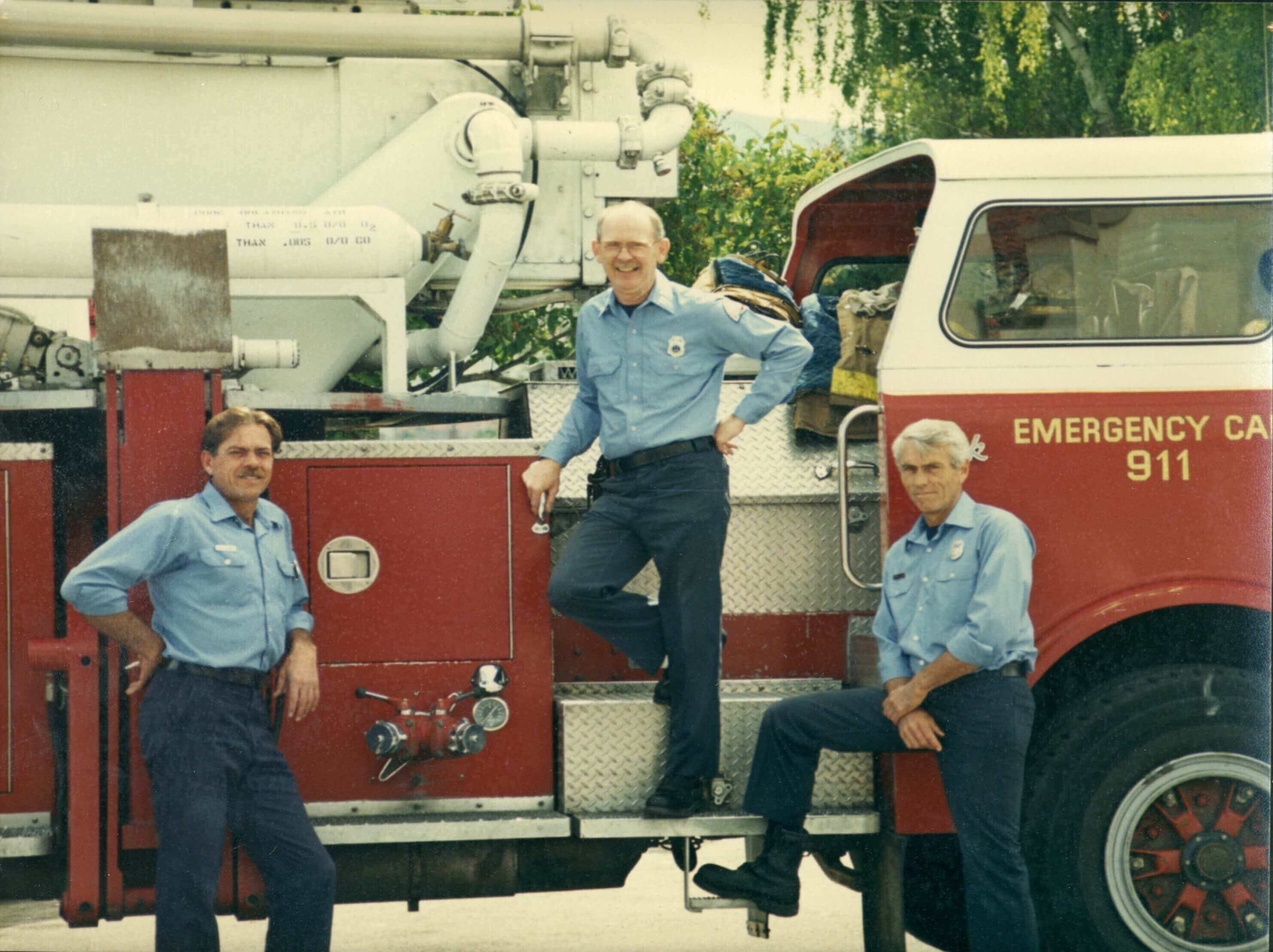 Red fire engine with three firefighters posing for camera