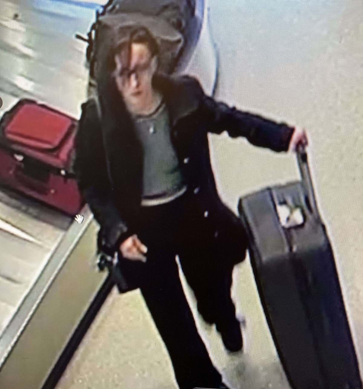 woman with dark hair and glasses walking in airport with black luggage