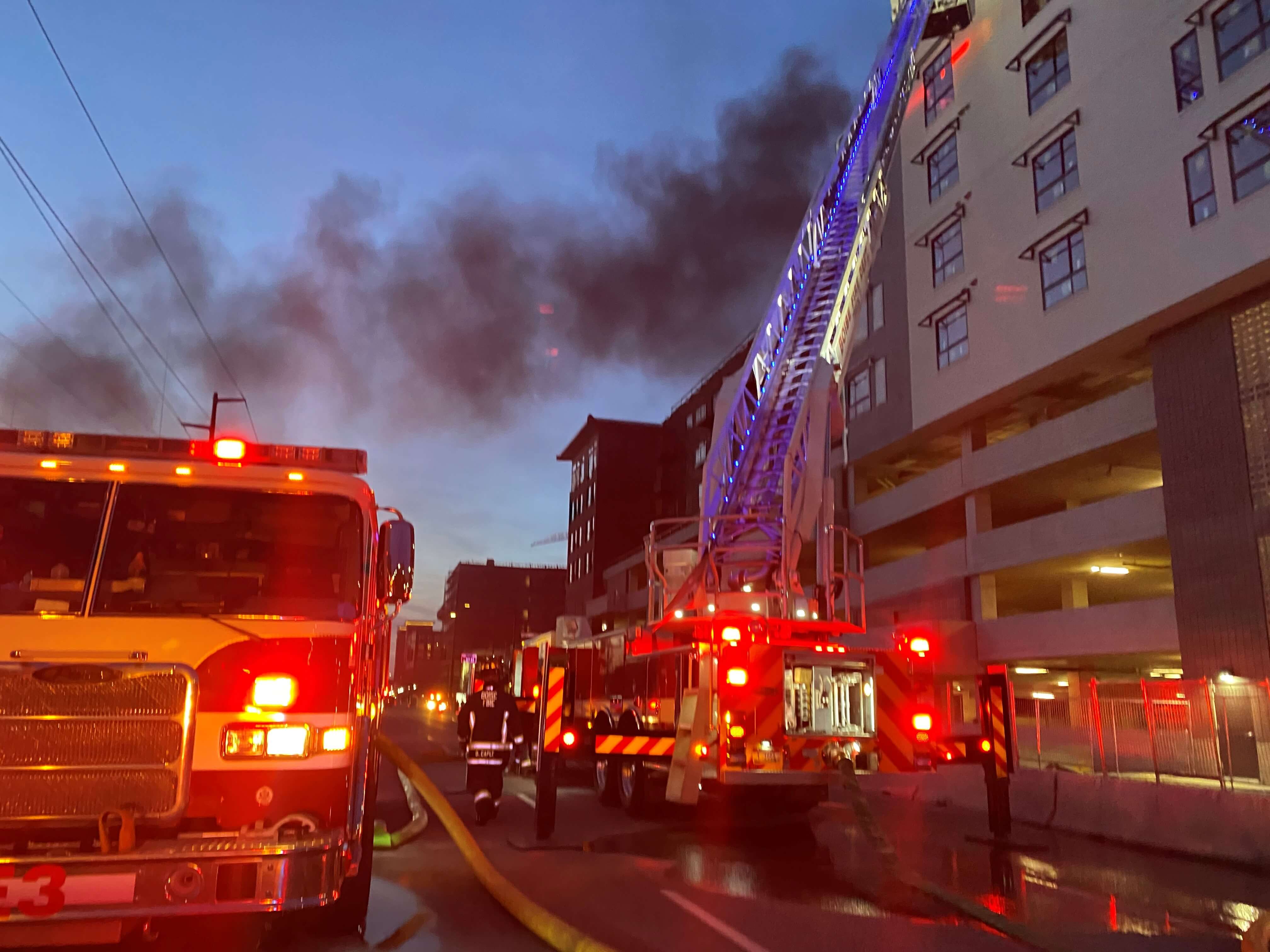 Fire trucks and a crane along a building with smoke coming out of the top
