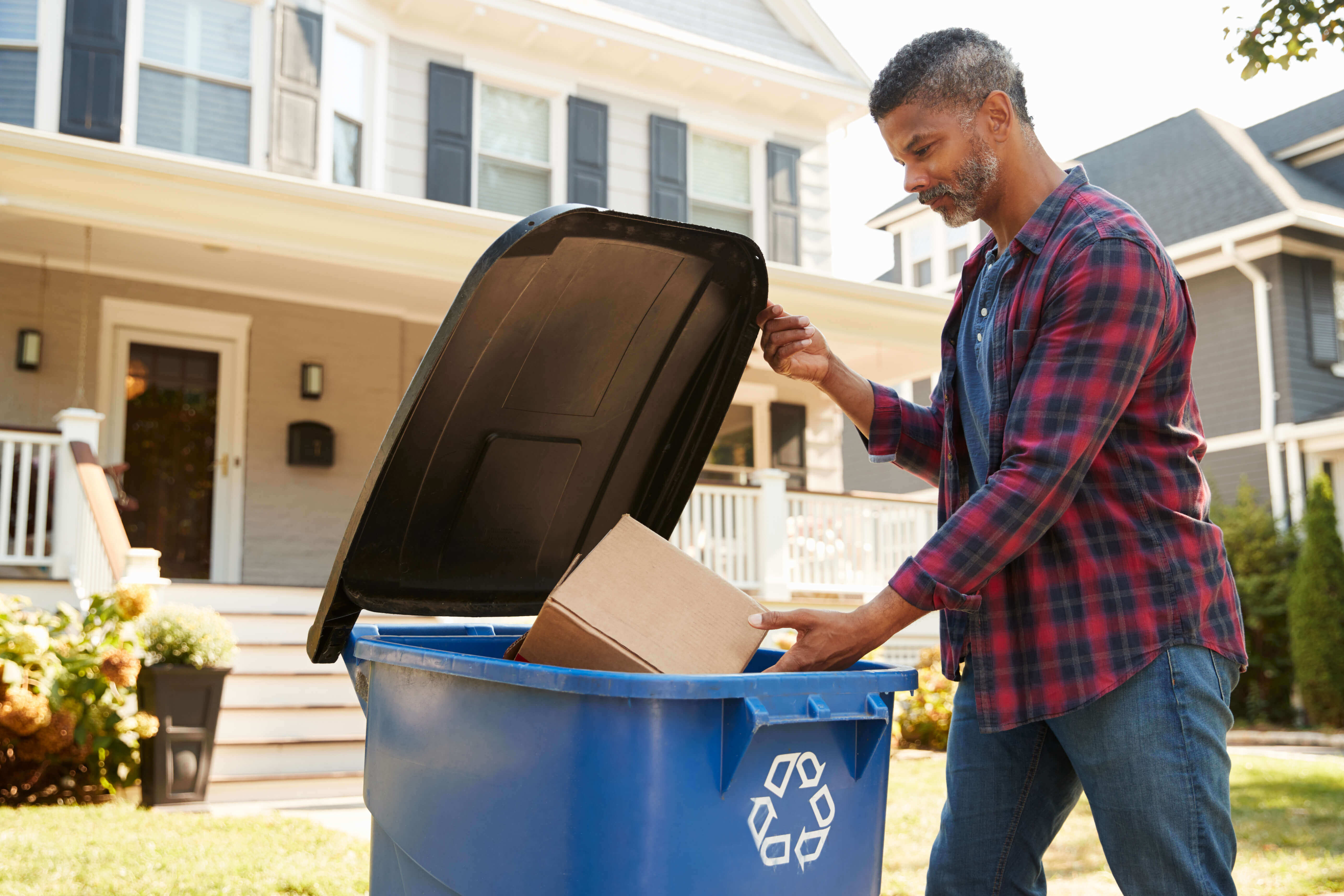 Man putting a cardboard box into a blue recycling bin