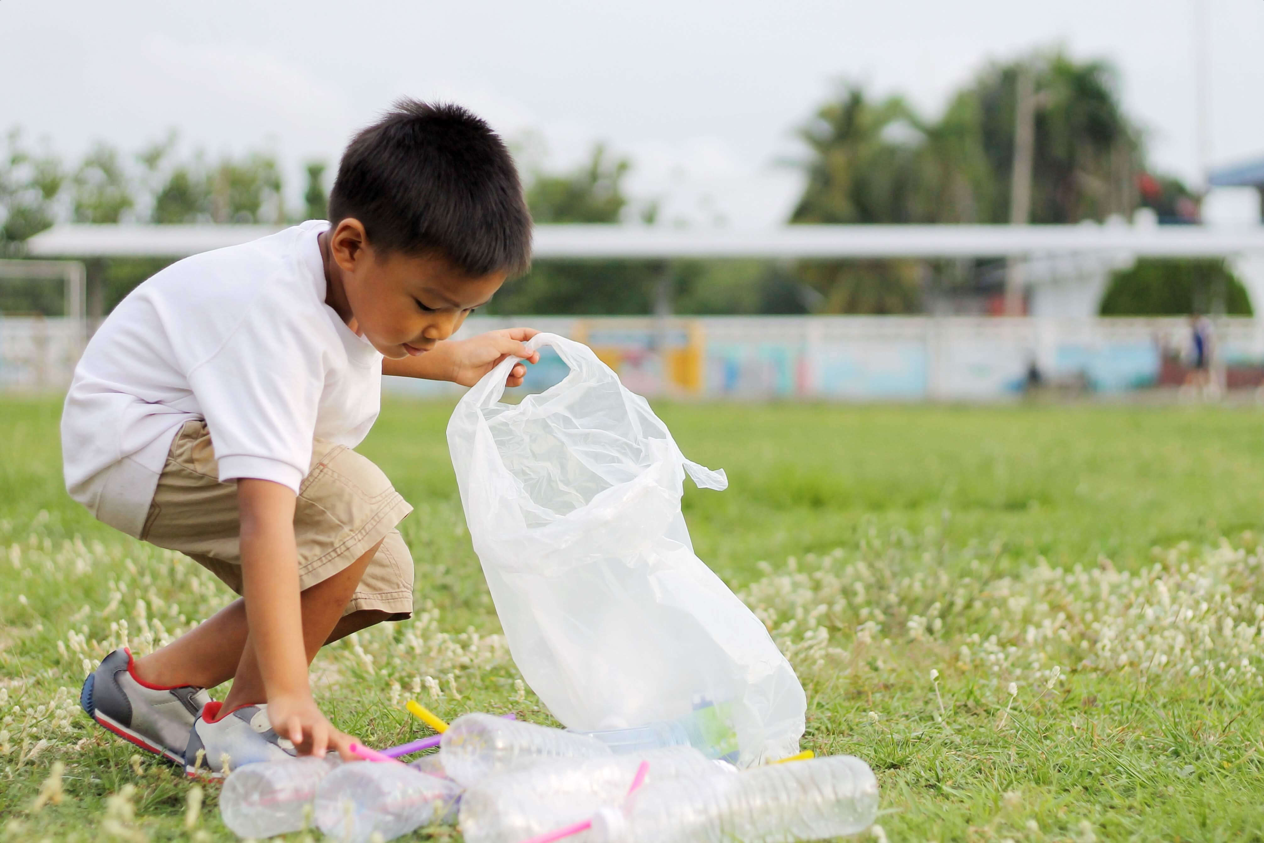 Little boy picking up garbage reusing a grocery bag