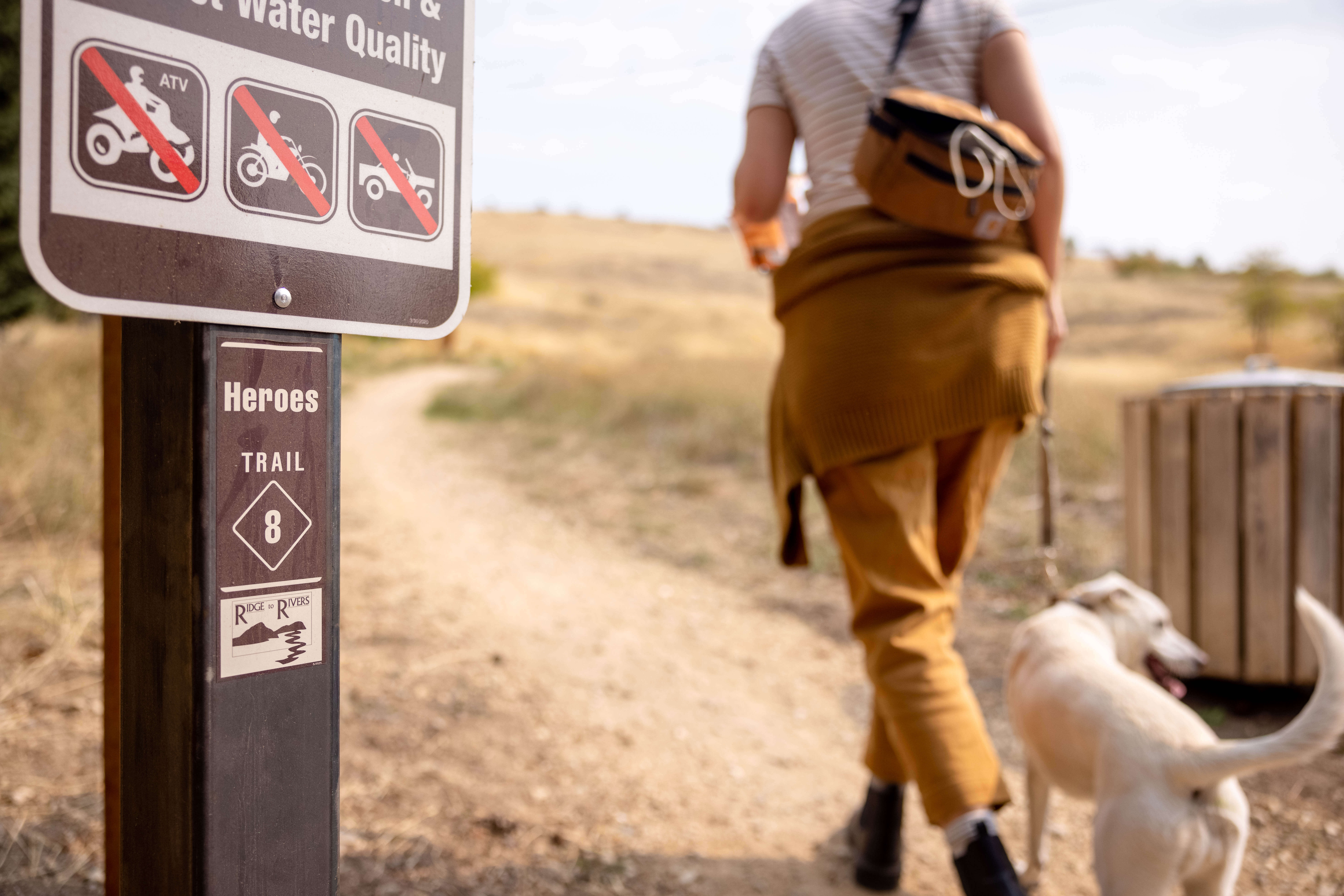 Woman walking dog on foothills trail with sign noting no cars on trails
