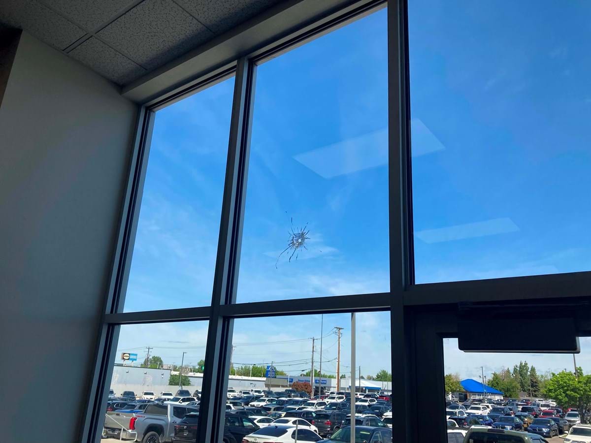 view of window looking from the inside with gunshot hole in it. Blue skies outside with cars parked in the parking lot.