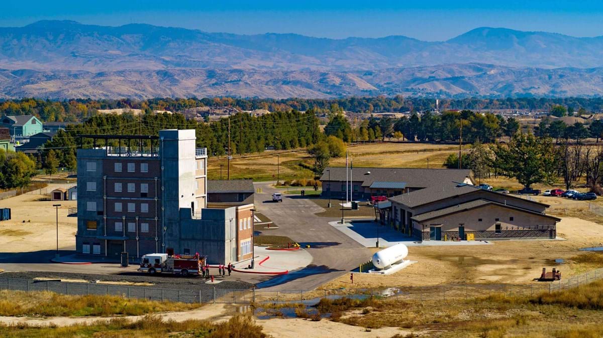 Aerial view of Fire Training Facility made up of three large buildings surrounded by dry grass and foothills in the background. 
