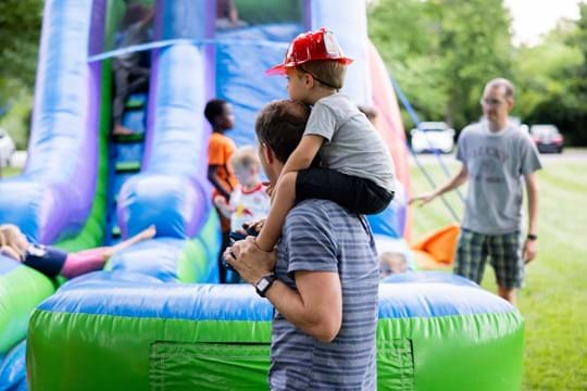 Little boy sitting on dads shoulders with kids on bounce slide behind them