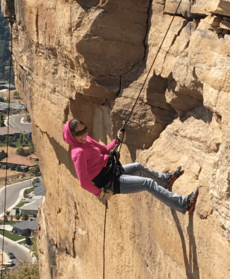 Woman wearing pink sweater scaling down cliff with harnesses