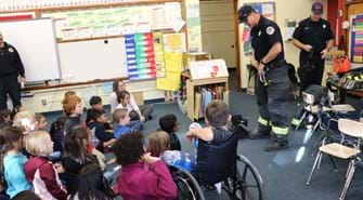 Firefighter stands in front of classroom of school aged children