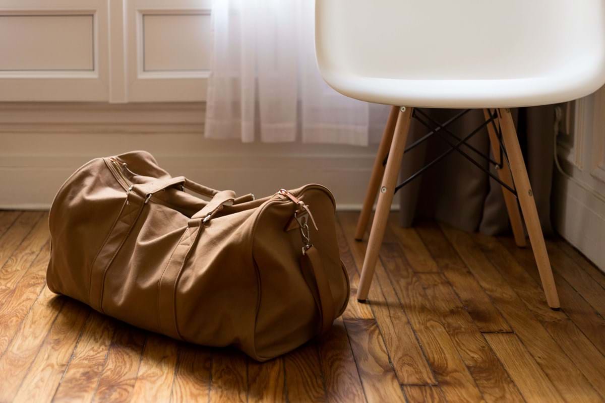 A duffle bag sitting next to a door and a chair.