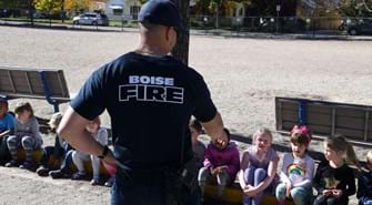 Kids sit on a curb with a Boise firefighter in front of them