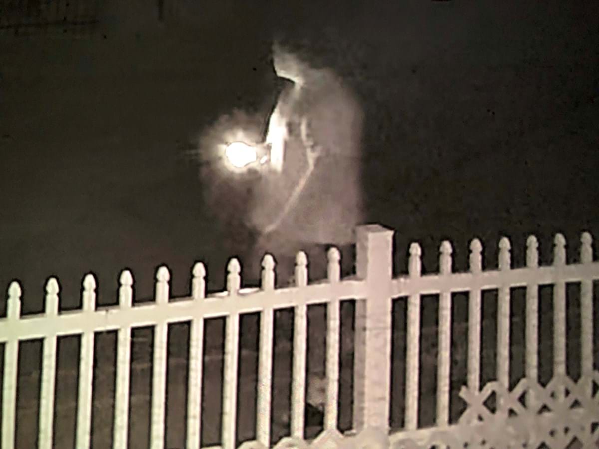 man standing in the dark behind a fence with a light in front of him 