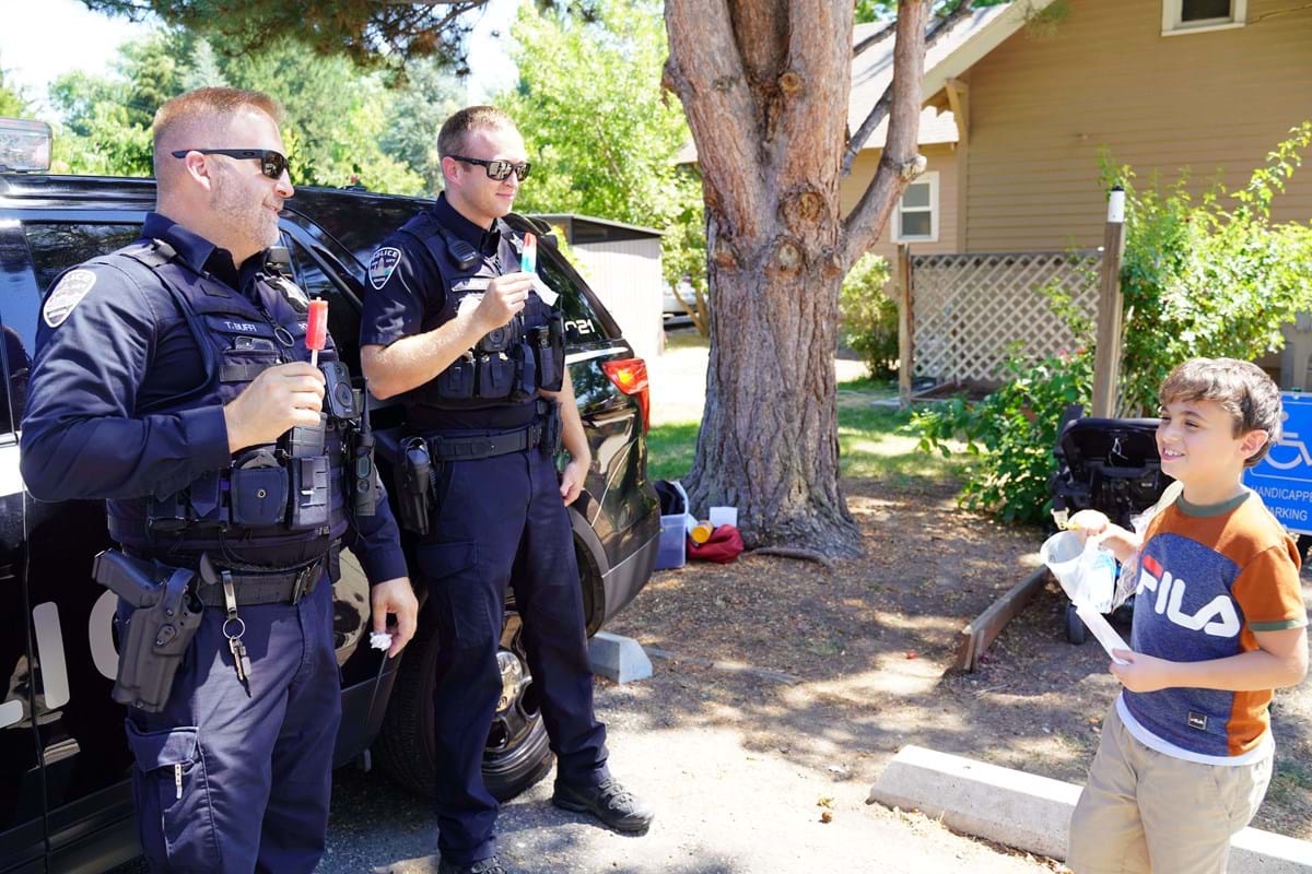 Two police officers eating popsicles and talking to a young boy