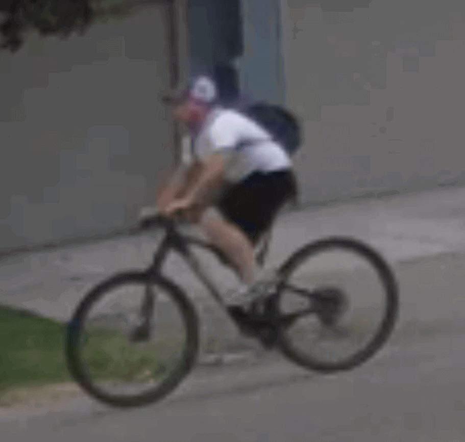 Man wearing a hat, white t-shirt and black shorts on a black bicycle.
