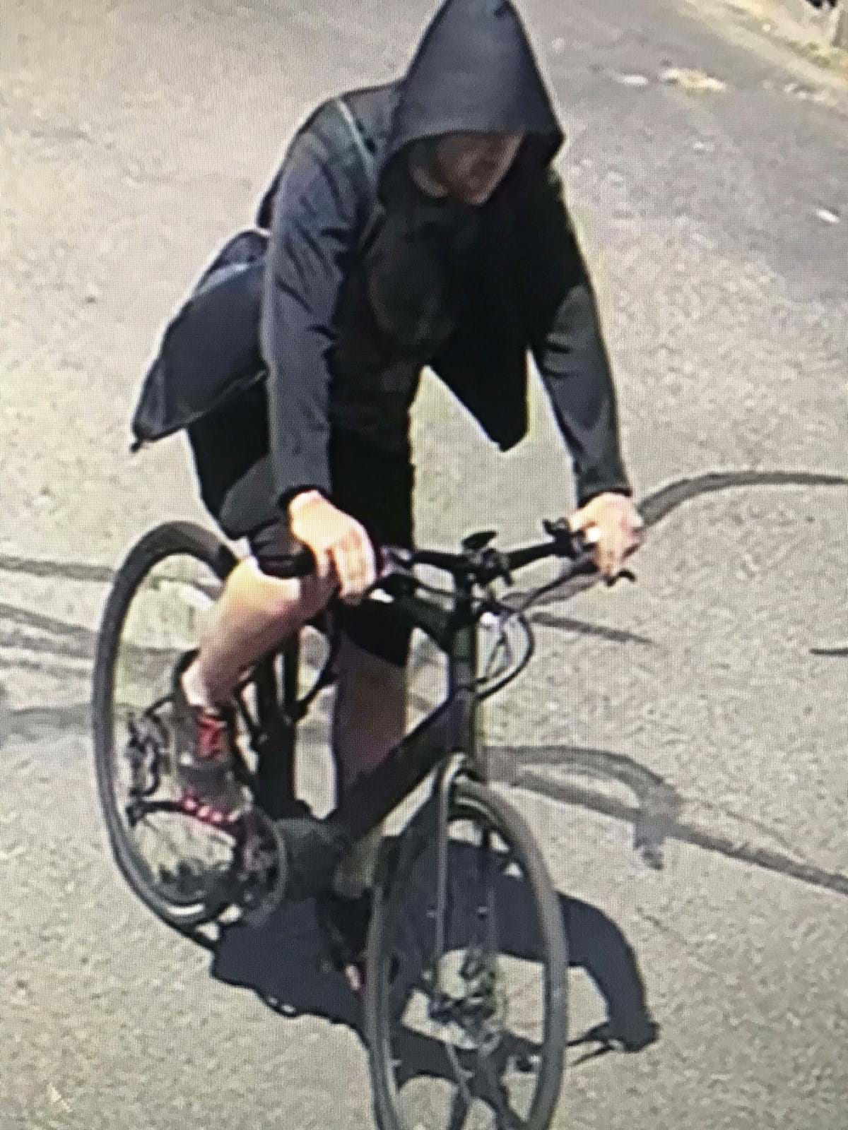 Man wearing a black hoodie and shorts riding a black bicycle.