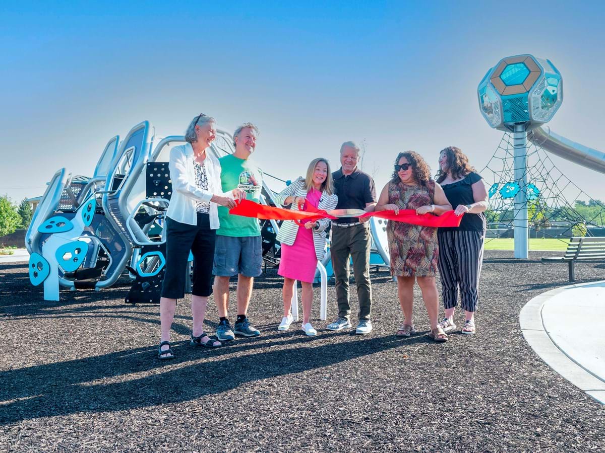 A group of 6, including Council President Elaine Clegg, Parks Director Doug Holloway, Council member Lisa Sanchez and Mayor Lauren McLean, at Franklin Park holding red ribbon with large scissors cutting the ribbon. 