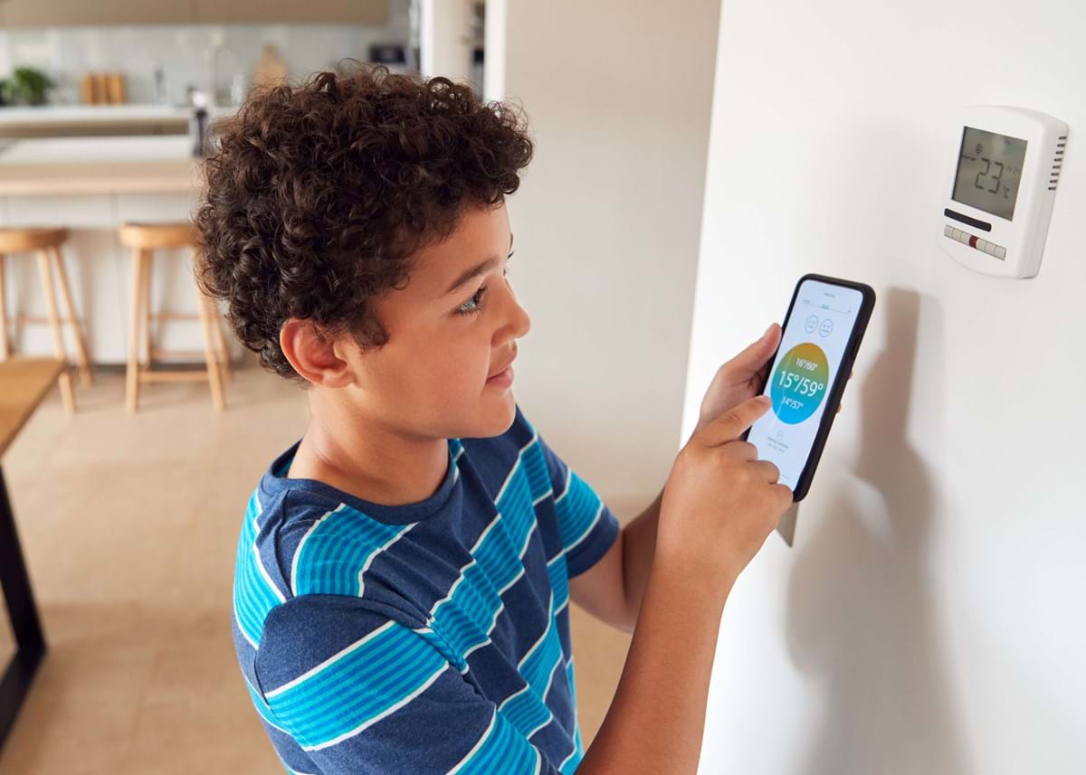 Boy adjusting a thermostat with a smart phone