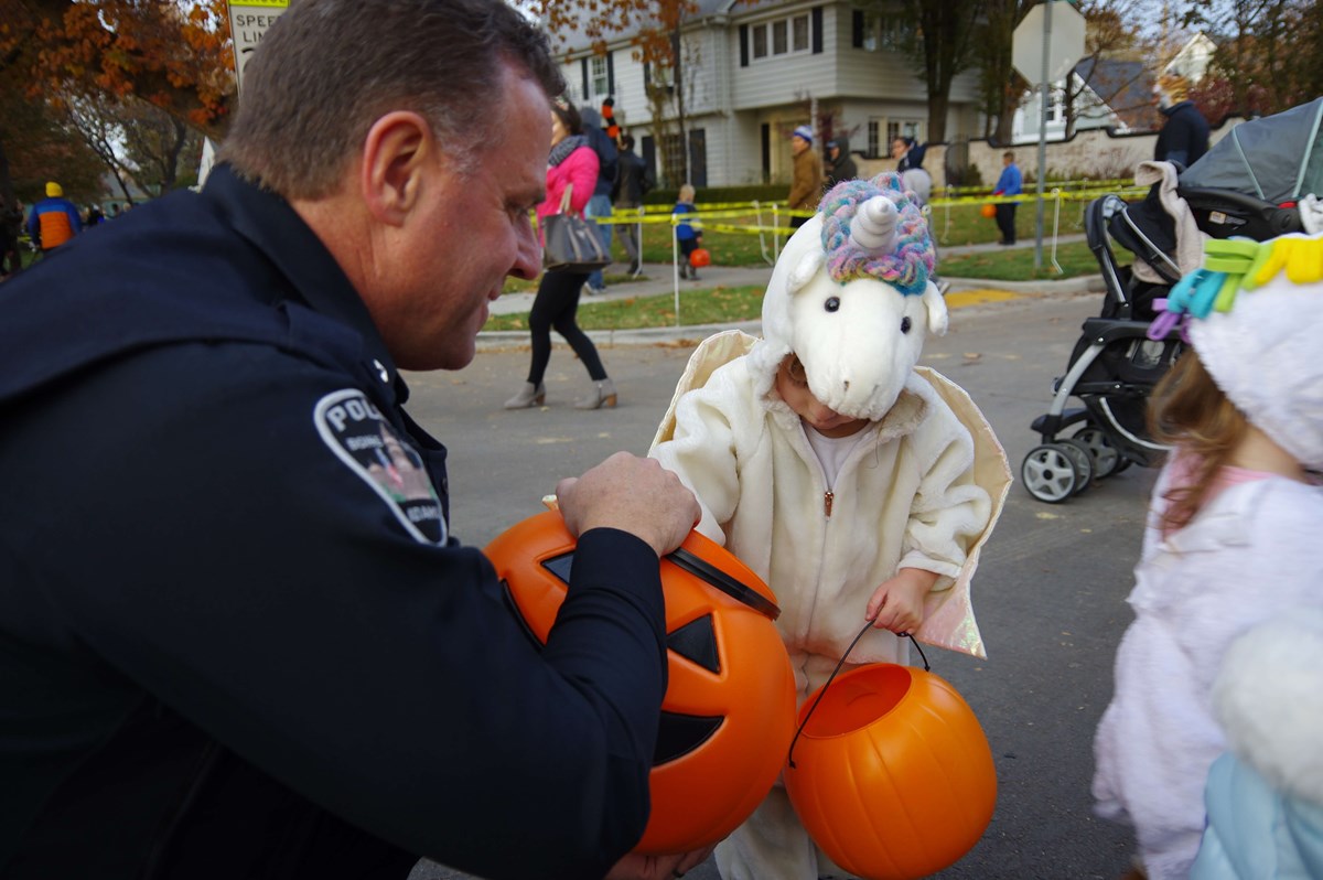 Police officer handing little girl dressed in a unicorn costume candy