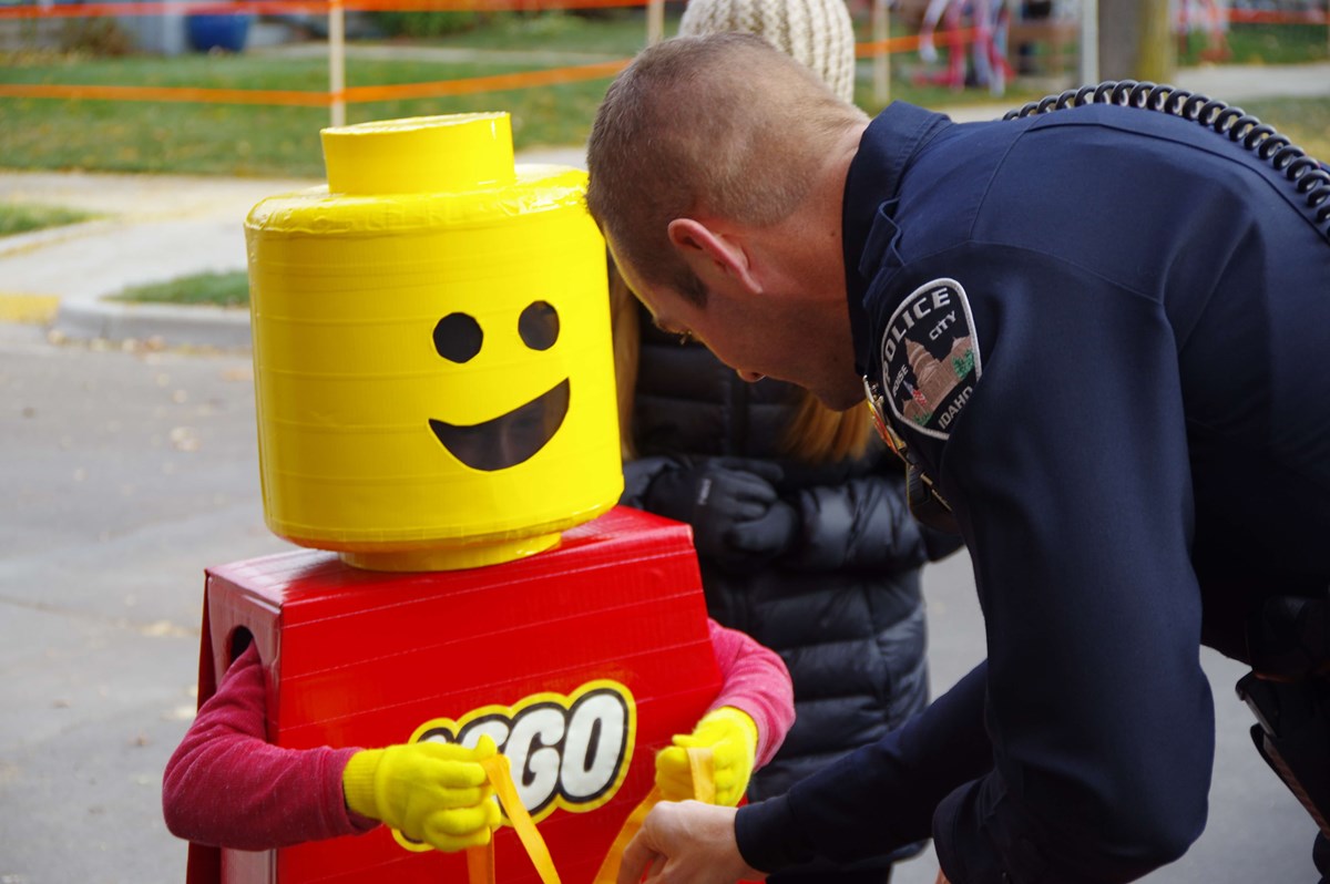 Little kid dressed as Lego character getting candy from police officer.