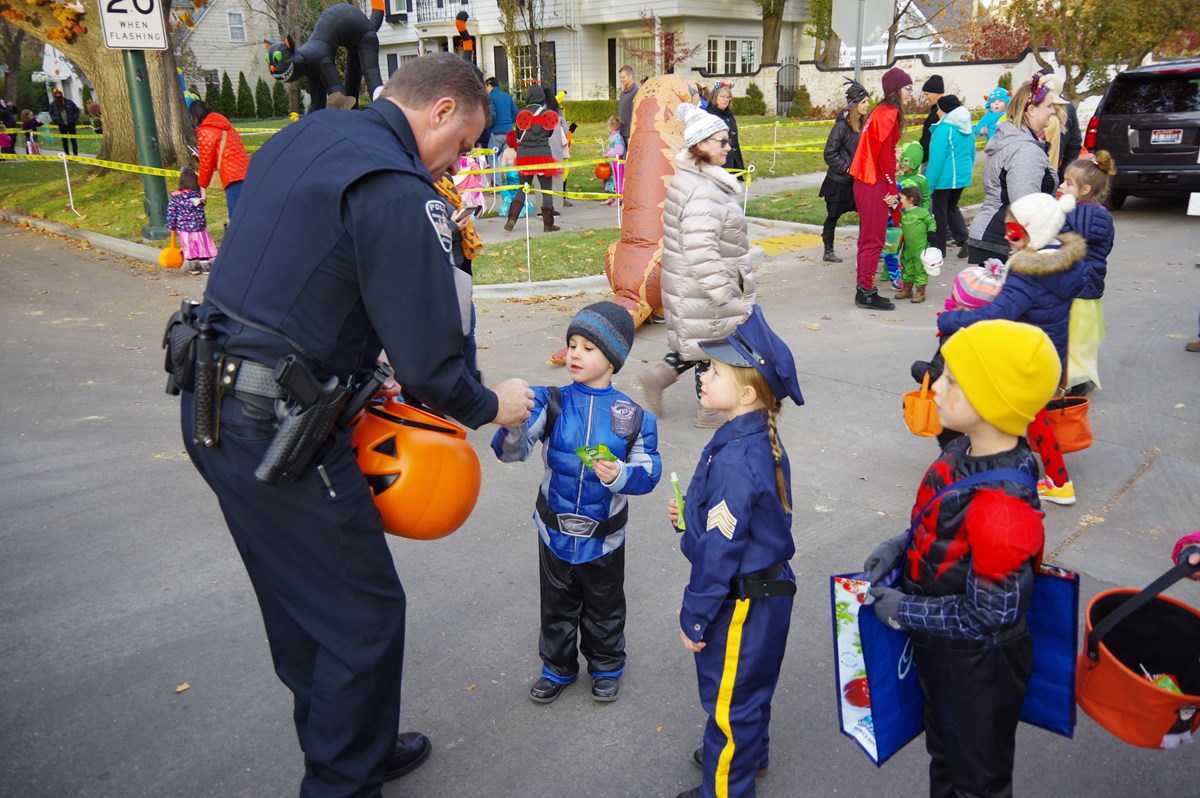 Police officer handing candy to little boy dressed in star trooper uniform, a little girl dressed as a police officer, and a little boy in super hero costume.