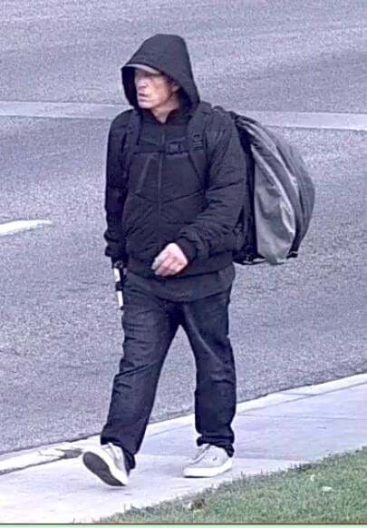 man with black jacket wearing his hood over a hat and backpack on his back walking down the street