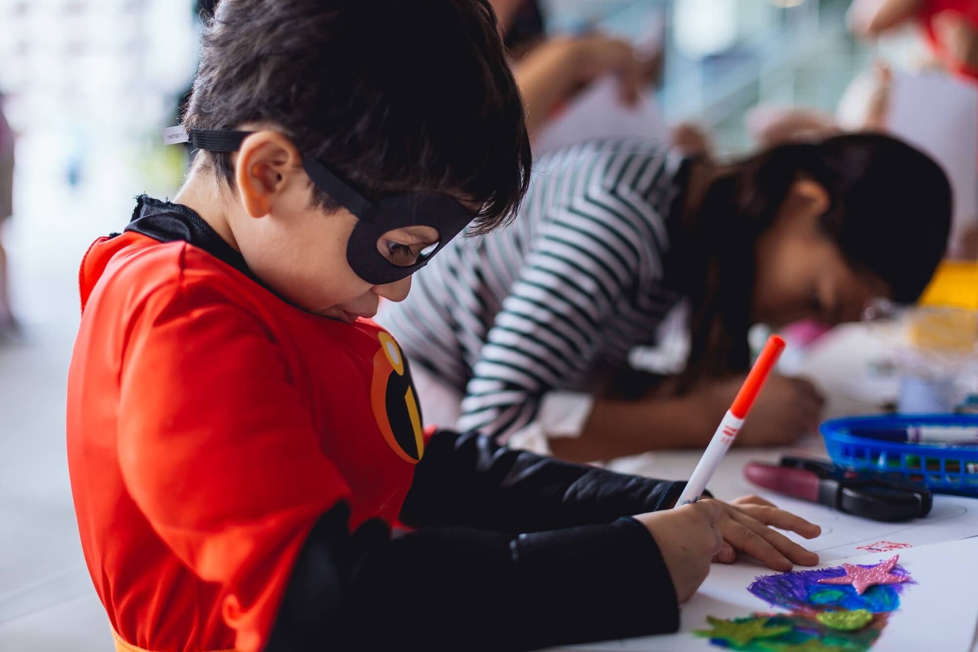 Child in a superhero costume and mask colors with a pen
