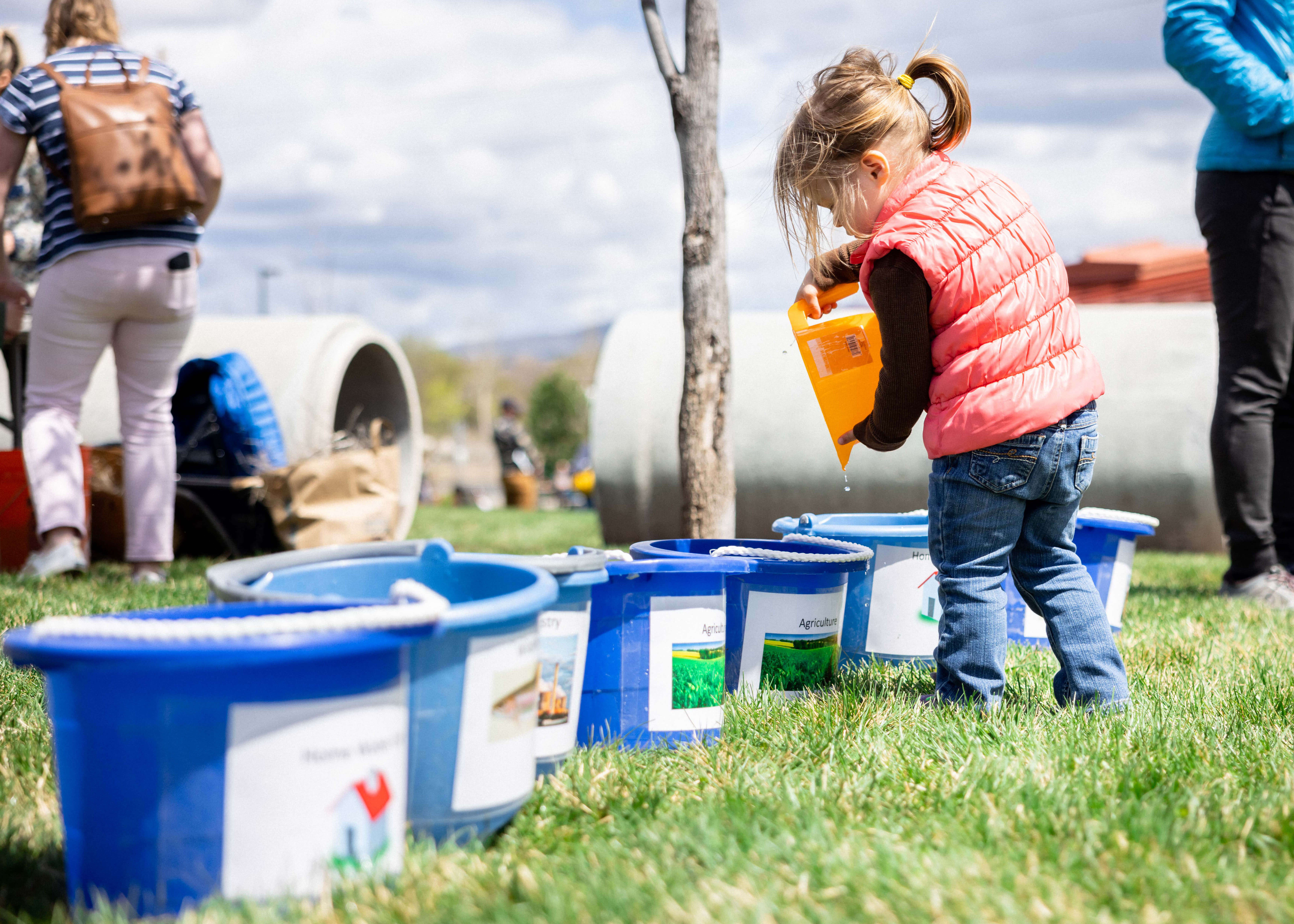 Small child standing next to blue buckets.