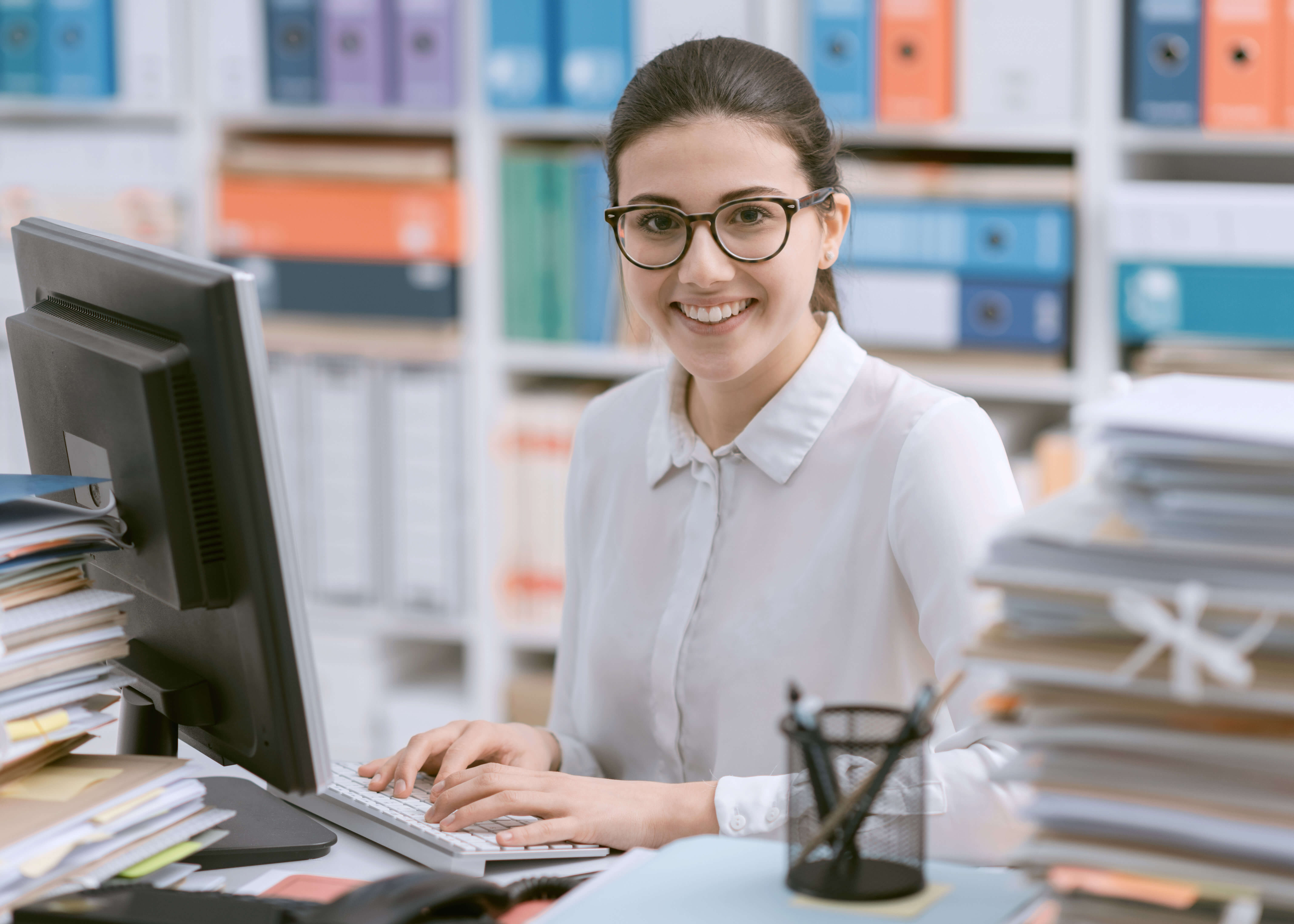 A woman works on a computer in an office full of records.