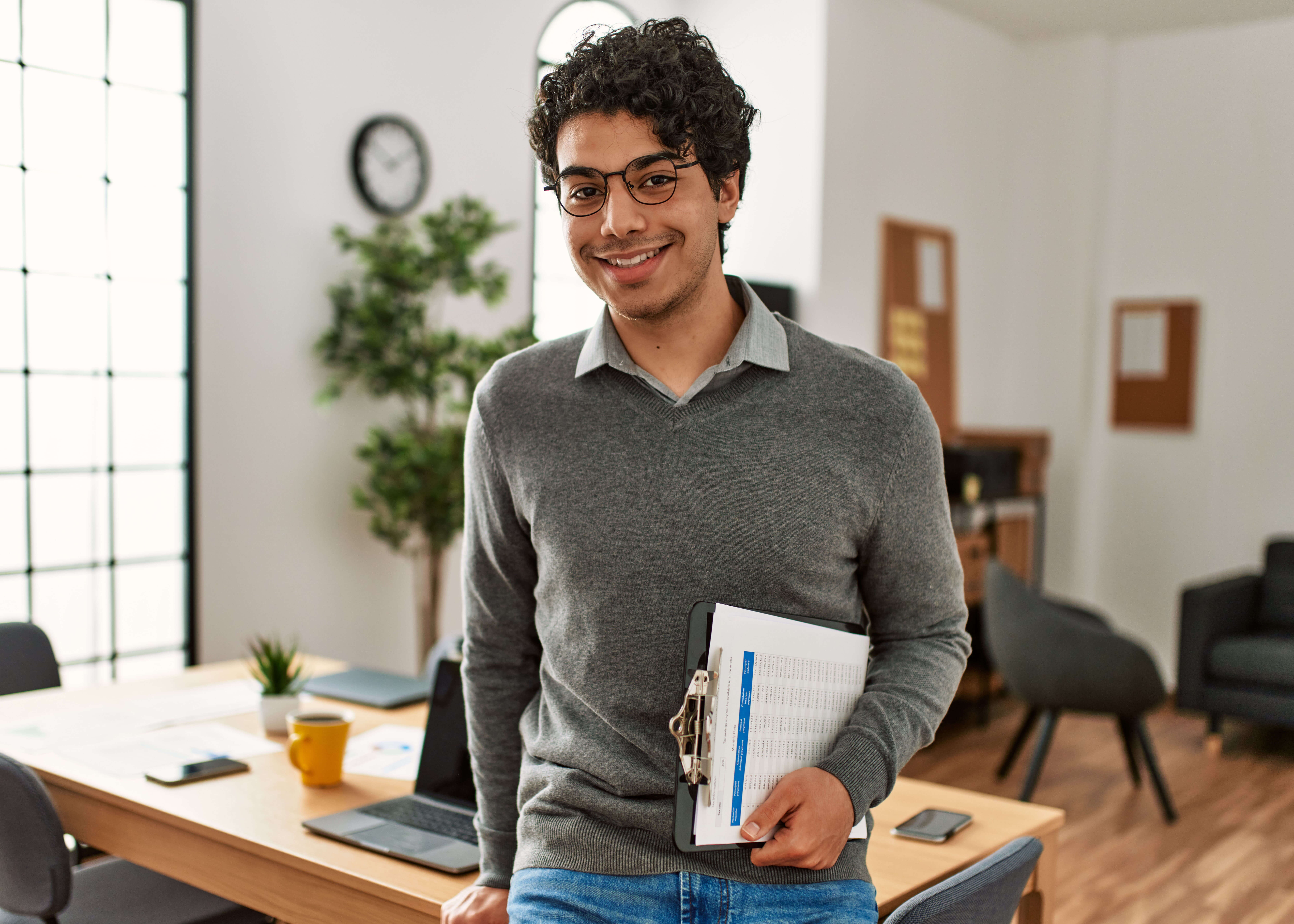 A man holding a clipboard stands in an office.