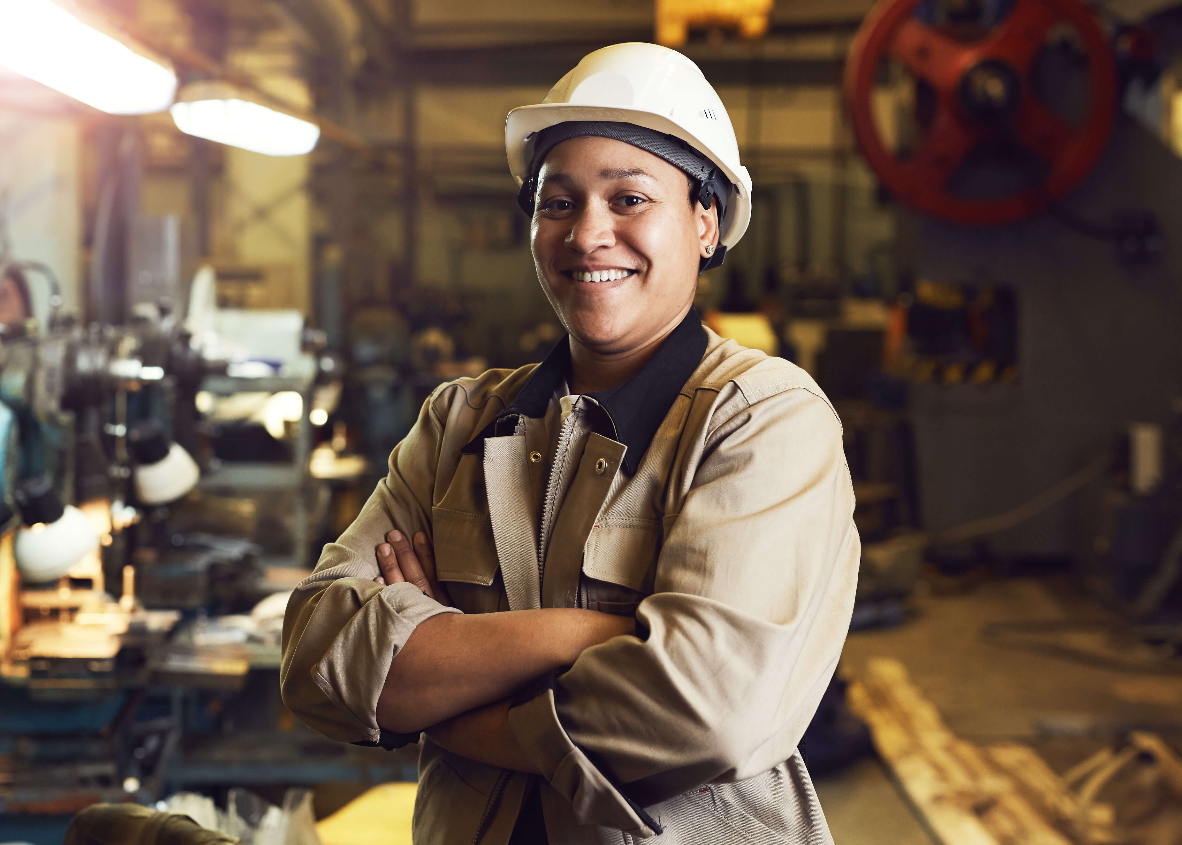 A mechanic in a hardhat stands in front of an industrial shop.