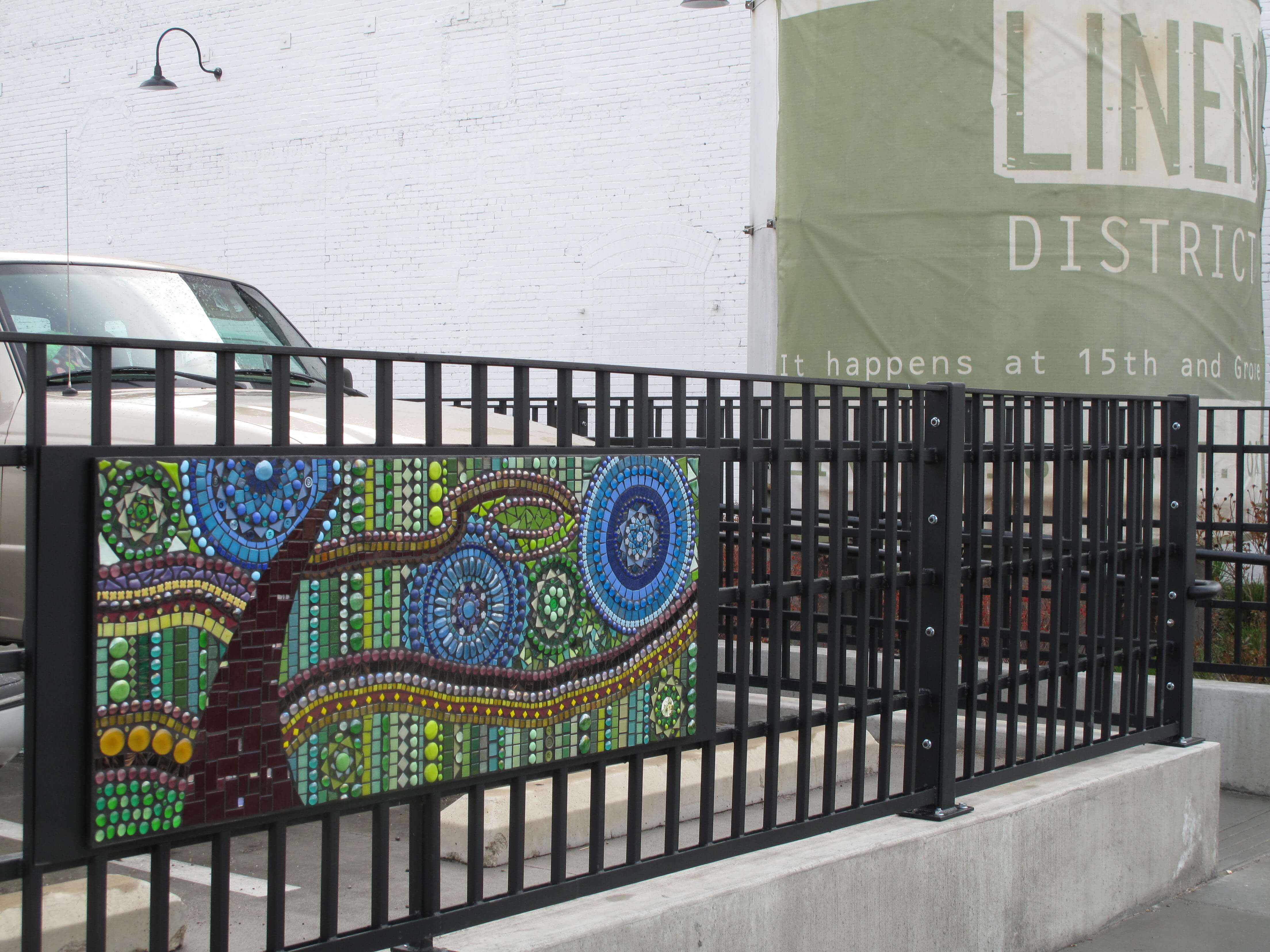 Black iron gate with tree and wind mosaic artwork in front of a Linen District banner.