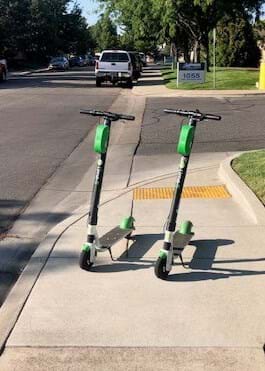 Two Lime e-scooters on sidewalk in neighborhood blocking pathway