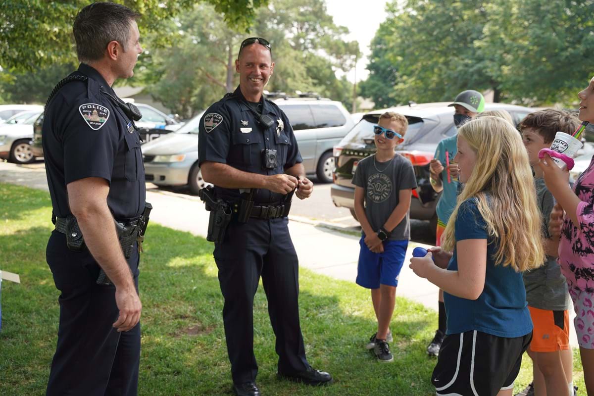 Two male officers standing with kids during summer and the children smiling